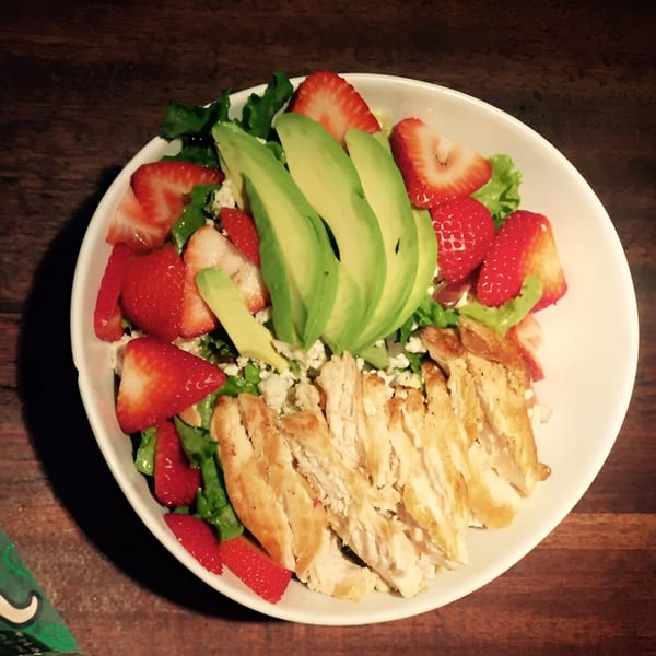 Chicken and strawberry salad with avocado slices and crumbled cheese on a white plate.