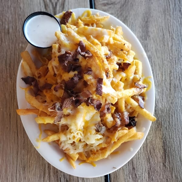 A plate of Irish pub fries with melted cheese, bacon bits, and a side of ranch.
