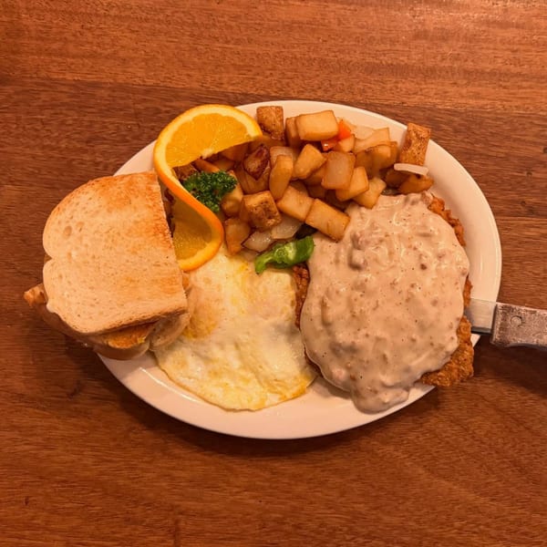 A hearty breakfast plate with chicken fried steak, gravy, fried eggs, home fries, toast, and orange slices.