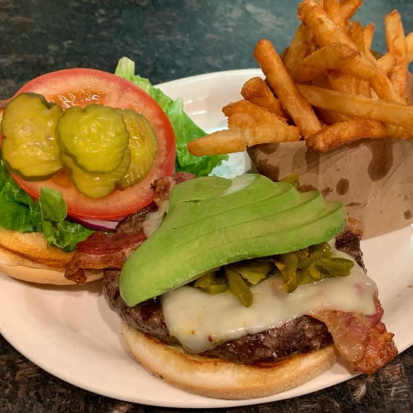 Vista Village Pub's burger with avocado, bacon, cheese, and jalapeños, served with fries.