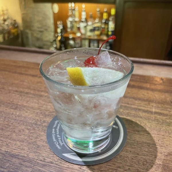 A refreshing cocktail with ice, lemon, and a cherry on a coaster at Vista Village Pub.