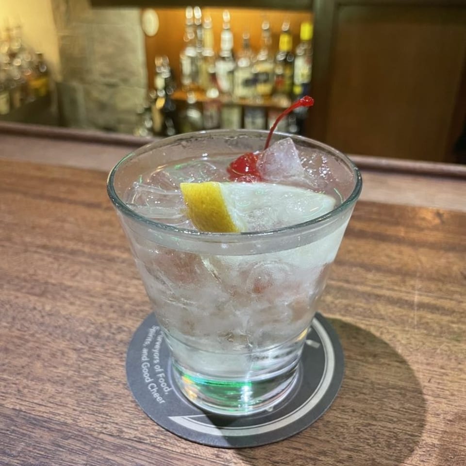 A refreshing cocktail with ice, lemon, and a cherry on a coaster at Vista Village Pub.