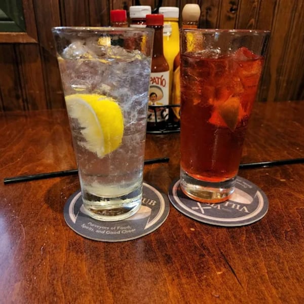 Two drinks, one clear with lemon and one amber, on coasters at Vista Village Pub.