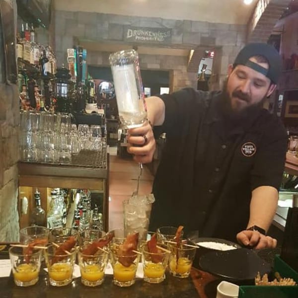 Bartender pouring a drink at Vista Village Pub, with bacon-garnished shots on the counter.